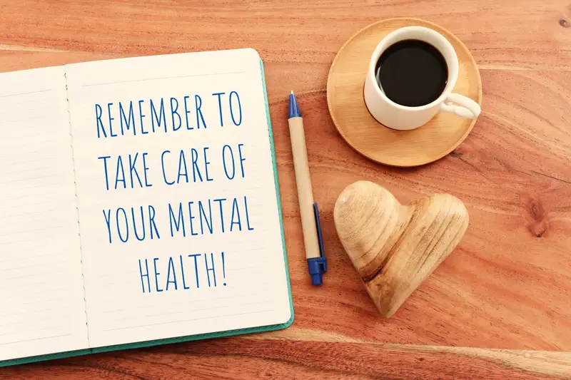 dilworth-center-remember-to-take-care-of-your-mental-health-01 Notebook with a reminder to take care of your mental health, next to a coffee cup and heart-shaped ornament, promoting addiction treatment and mental health awareness.