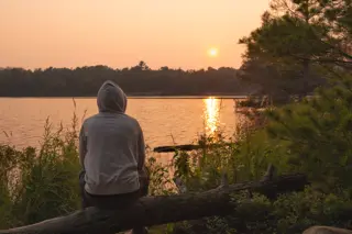 drug-relapse-contemplation-lake-sunset A person sitting alone at a lake during sunset, reflecting on their recent drug relapse.