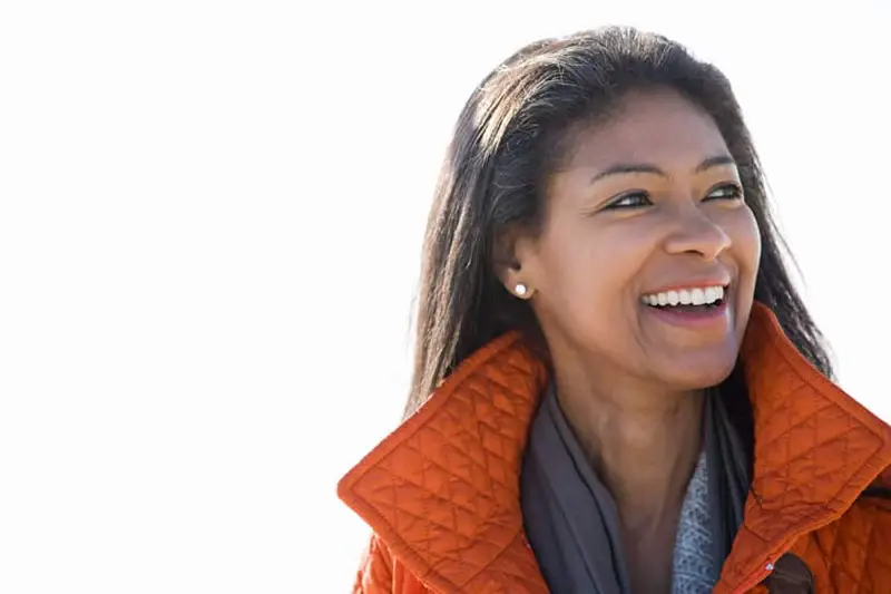 smiling-woman-addiction-treatment-charlotte Smiling woman in an orange coat, representing positive outcomes from addiction treatment in Charlotte.
