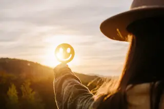 well-being-sunrise-smiley-face A woman holding a smiley face against the sunrise symbolizes her positivity and well-being.
