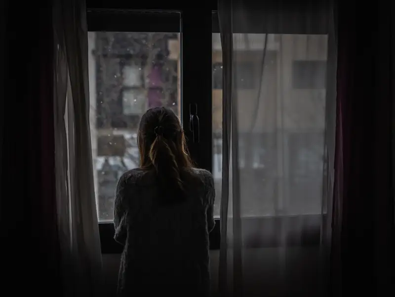 benzo-addiction-withdrawal-detox-xanax-dependence-anxiety-treatment A woman stands by a window, looking out into a dreary, overcast scene, symbolizing the isolation and struggle often experienced during benzo withdrawal and addiction recovery.