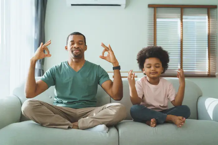 family-therapy-drug-addiction-young-adult-rehab-outpatient-drug-treatment A father and child meditating together on a couch, symbolizing the role of family therapy in drug addiction recovery for young adults.