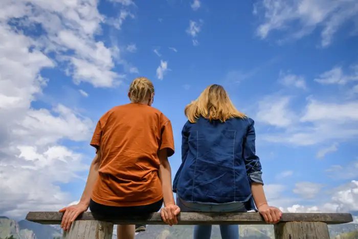 outpatient-drug-rehab-near-me-family-addiction-support-teenager-rehab Two individuals sitting on a bench, gazing at a bright blue sky, symbolizing the importance of family support in the rehabilitation journey for young adults and teenagers.