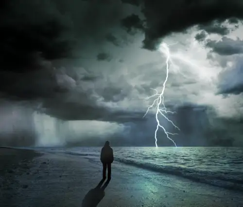 A person standing on a dark beach as a lightning storm brews over the ocean, symbolizing the tumultuous and dangerous rise of crack cocaine addiction.