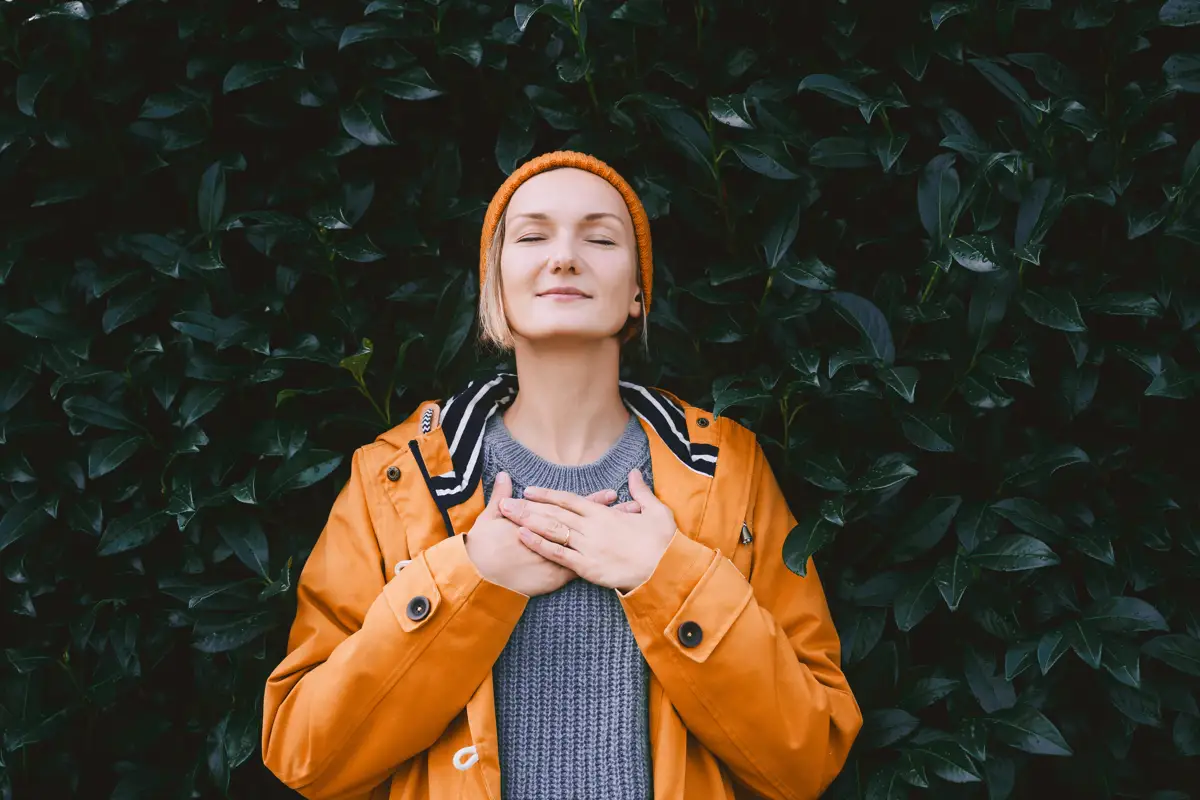 woman-meditating-green-leaves-anxiety-management Woman in orange jacket meditating peacefully against a green leafy background, illustrating natural methods of calming anxiety without benzos.